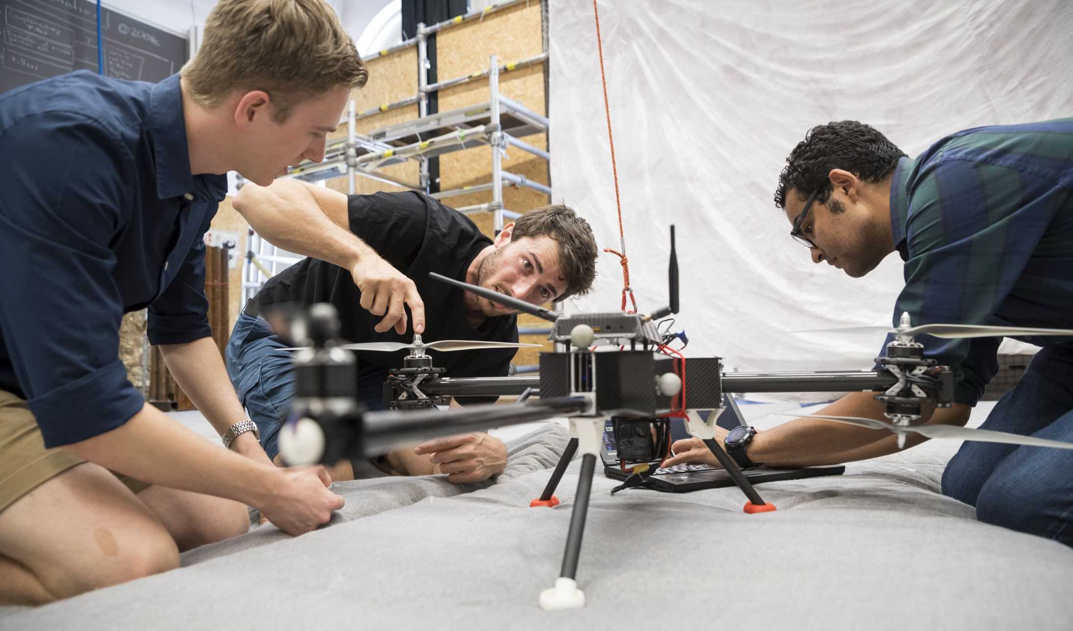 Timo Müller, Christian Sprecher and Kamel Mina kneeling on the floor, working on a drone